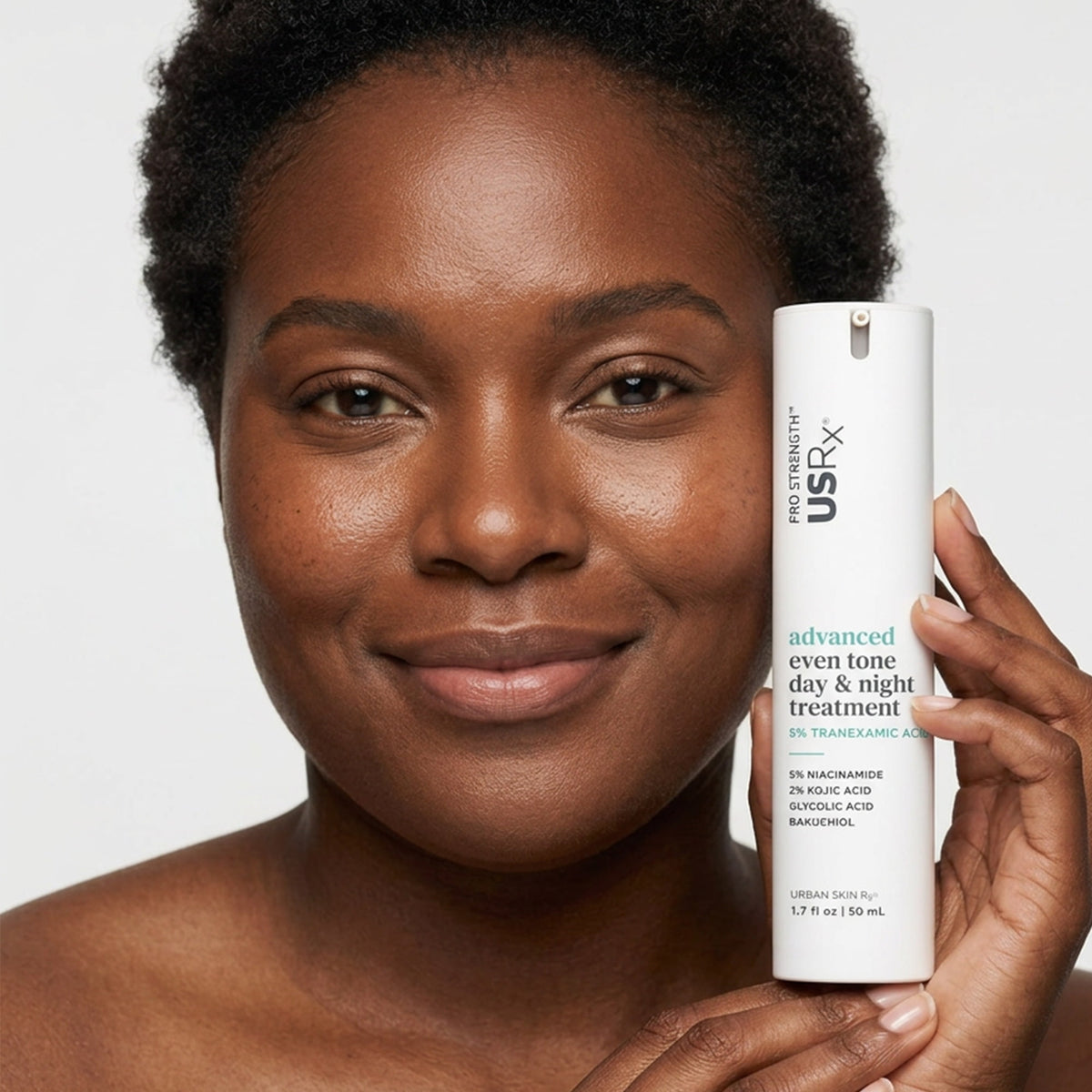 Woman holding a bottle of USRx Advanced Even Tone Day & Night Treatment near her face against a white background
