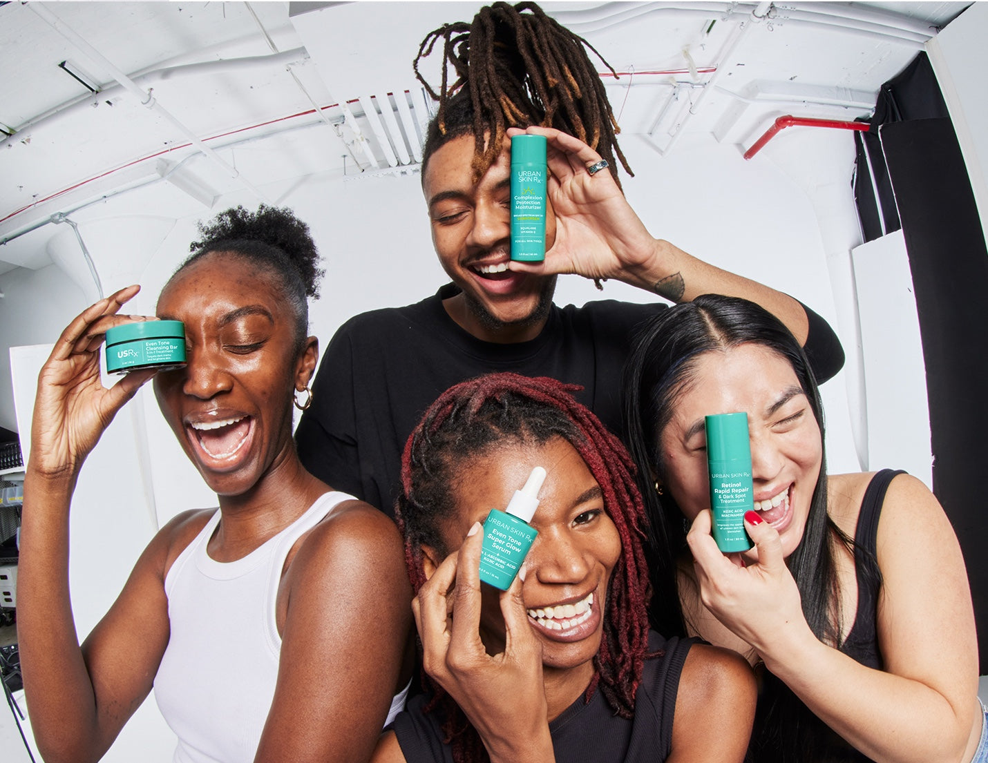 Four people smiling and holding different USRx skincare products against a white background