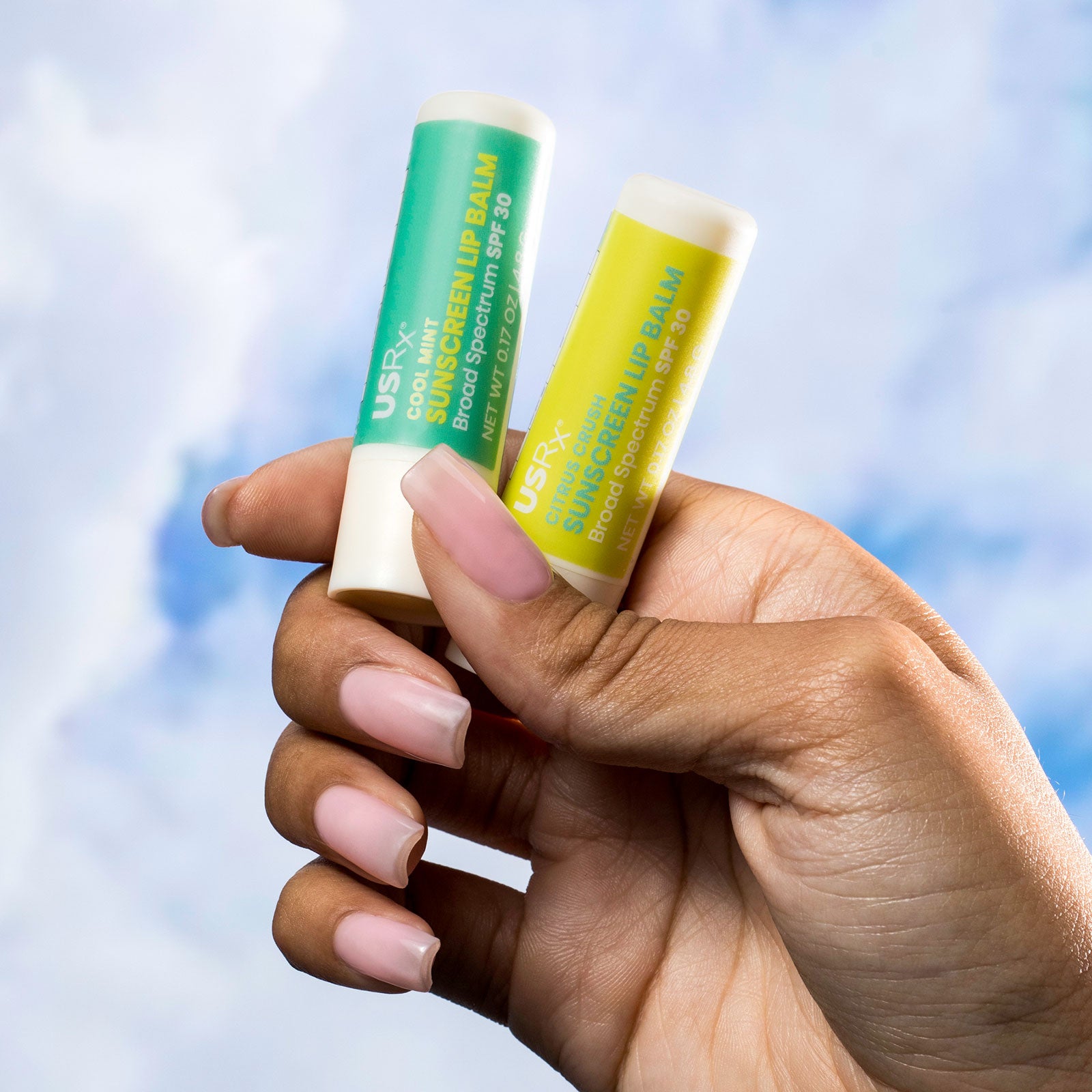 Woman holding tubes of USRx Sunscreen Lip Balm on a light blue background