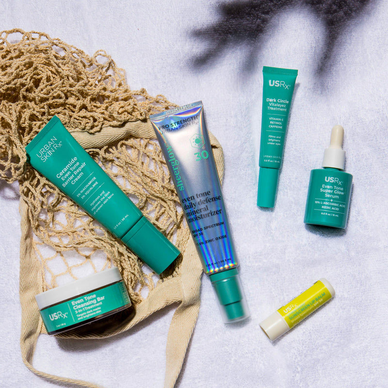 Urban Skin Rx Summer Essentials Bundle featuring six skincare products for a full A.M. and P.M. routine on a textured surface with a net bag.