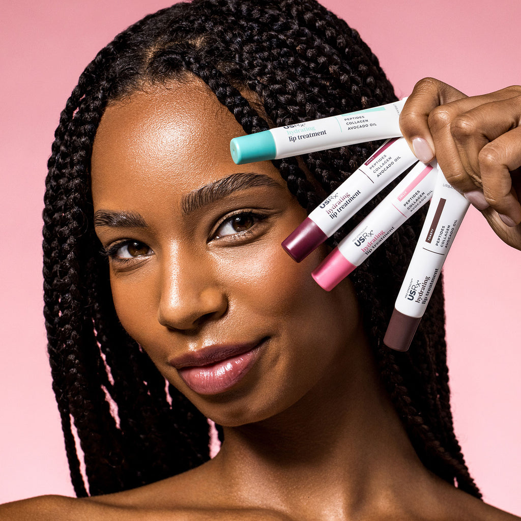 Smiling woman holding 4 different shades of USRx Hydrating Lip Treatment in Original, Jelly, Toasty and Juicy