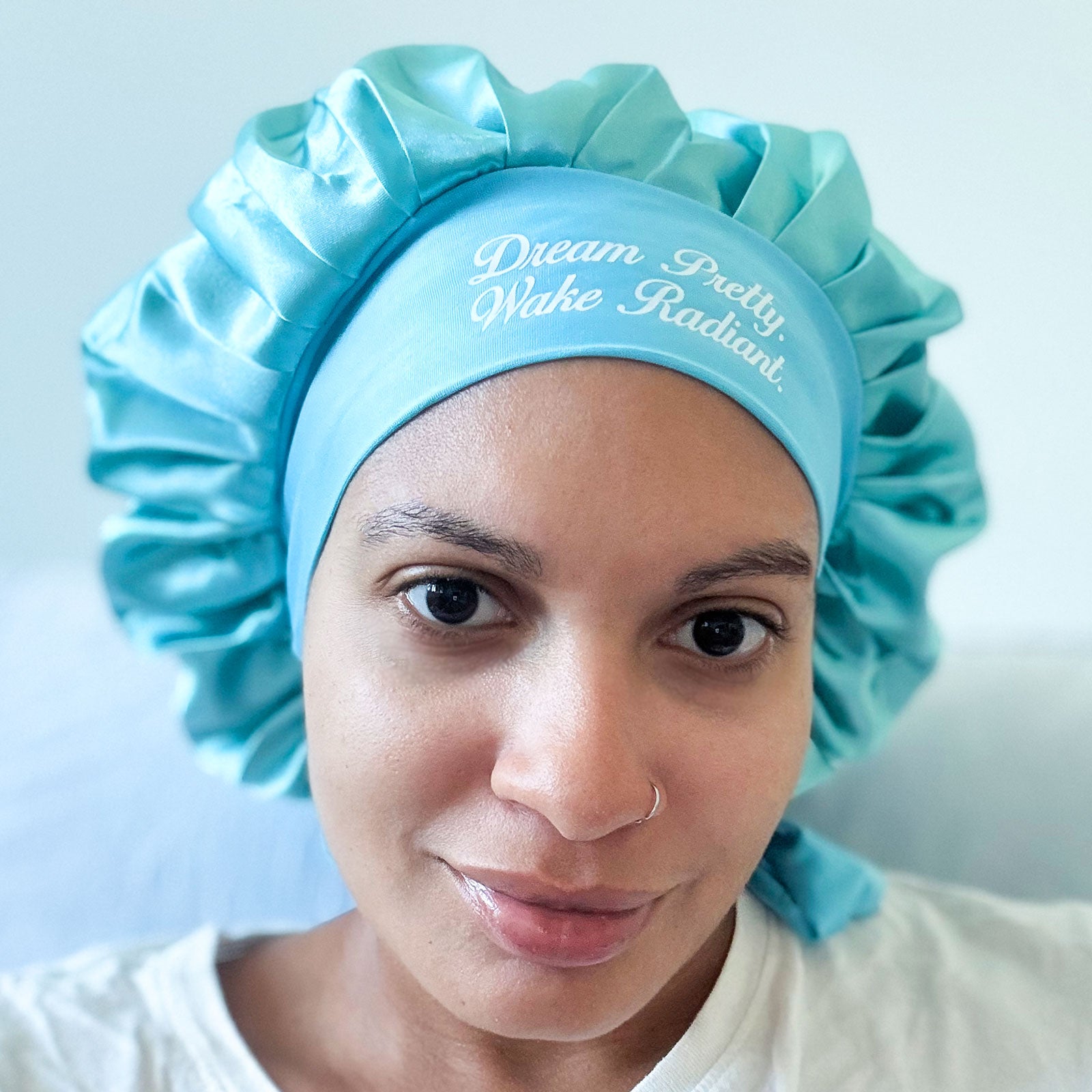 Smiling woman wearing blue satin bonnet that says "Dream Pretty, Wake Radiant" on the headband