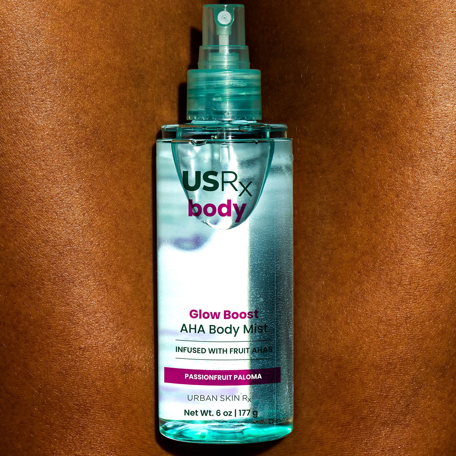 Bottle of USRx Glow Boost AHA Body Mist in Passionfruit Paloma shown on a woman's leg