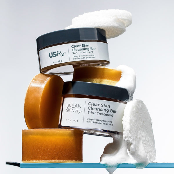 Two jars of USRx Clear Skin Cleansing Bar stacked on a shelf on a neutral background