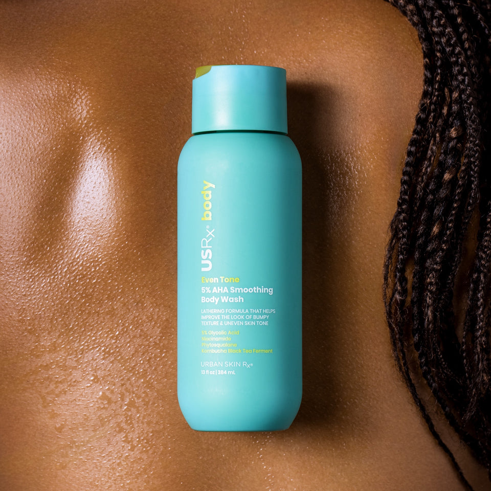 Bottle of USRx Even Tone 5% AHA Smoothing Body Wash shown on top of a woman's back
