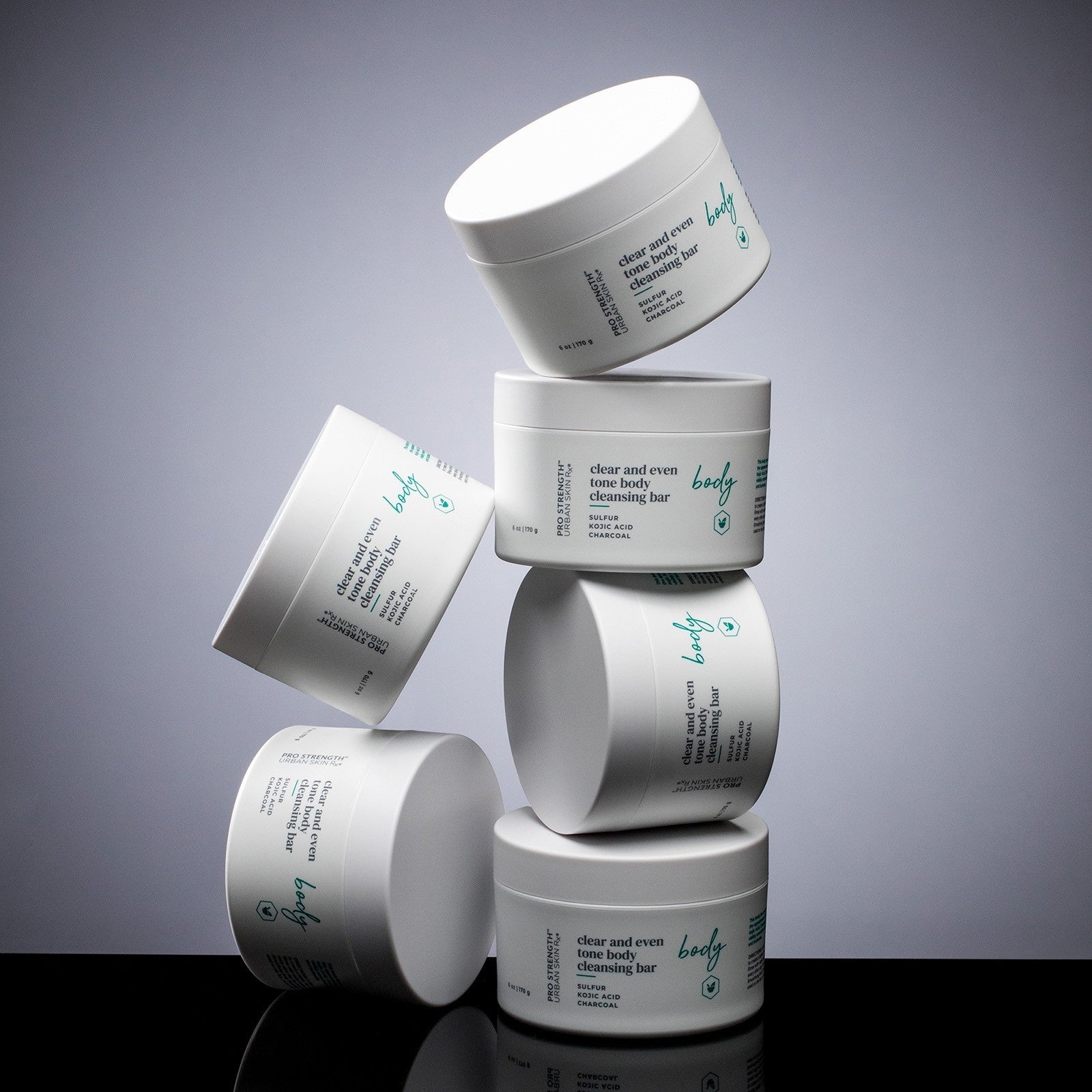 Multiple Jars of USRx Clear and Even Tone Body Cleansing Bar on a grey background