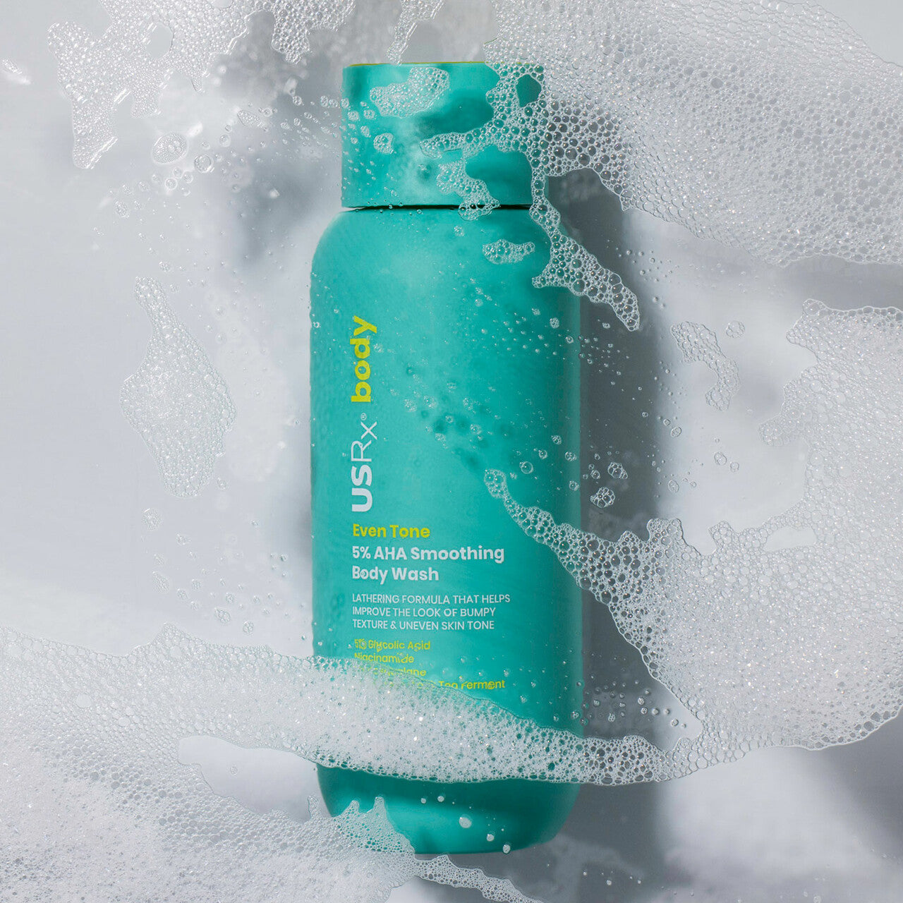 Bottle of USRx Even Tone 5% AHA Smoothing Body Wash surrounded by suds