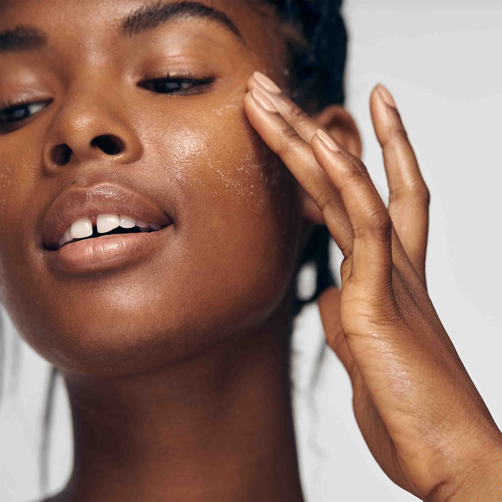 African American model exfoliating her face with Lacticglow Micropolish Gentle Cleansing Gel
