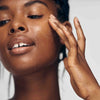 African American model exfoliating her face with Lacticglow Micropolish Gentle Cleansing Gel
