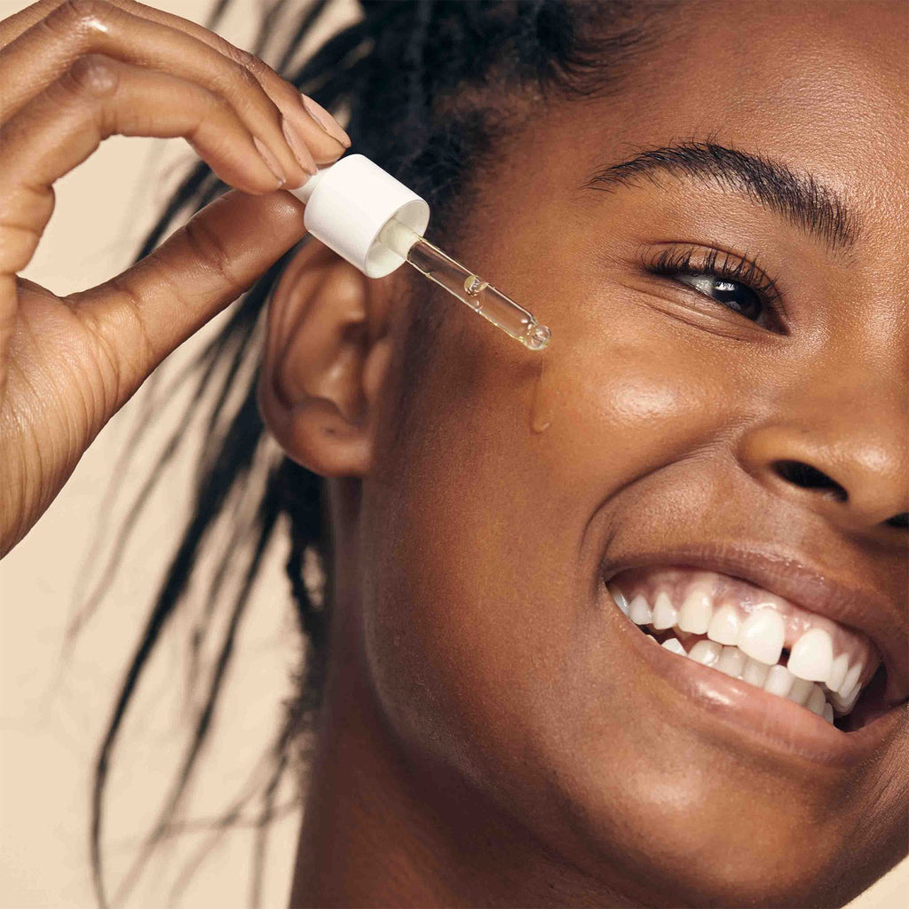 African American model using dropper to apply Reti- Glow Resurfacing Night Oil to her face